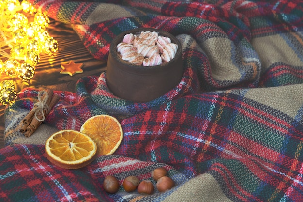 Grande tazza di cioccolata calda con marshmallow, cannella e arancia secca e coperta calda su un vecchio vintage in legno e luce di Natale. Accogliente sistemazione natalizia o autunnale.