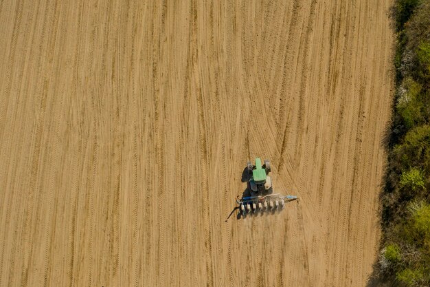 Grande trattore di vista aerea che coltiva un campo asciutto.