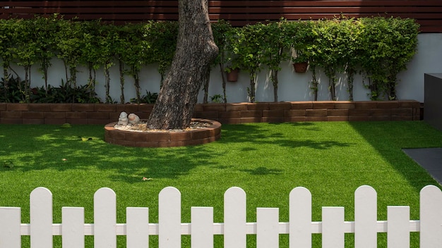 grande tronco d'albero su erba artificiale nel cortile anteriore con una recinzione di legno bianca sfocata in primo piano