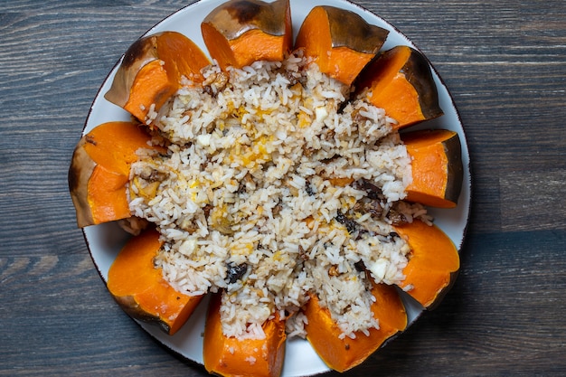 Grande zucca al forno con un primo piano di riempimento su un piatto, vista dall'alto. Zucca all'arancia arrosto farcita, intera al forno, farcita con una gustosa miscela di riso, uvetta e spezie