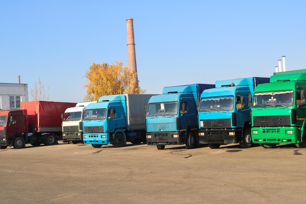 Grandi autocarri per carichi pesanti con cabine e rimorchi sono in fila pronti per la consegna del carico presso la raffineria industriale sullo sfondo del negozio di logistica per il trasporto di tubi