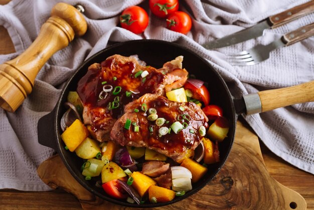 Grandi bistecche di maiale spalmate con salsa barbecue poggiano su grossi pezzi di verdure in una padella di ghisa