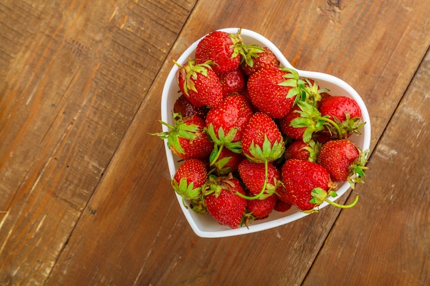 Grandi fragole fresche in un piatto bianco a forma di cuore sul tavolo. Foto orizzontale