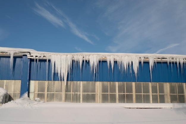 Grandi ghiaccioli sul tetto di una casa a schiera in una nevosa giornata invernale tra il disgelo Pulizia del tetto da neve e ghiaccioli