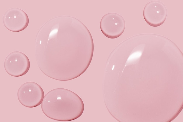 Grandi gocce di gel d'acqua liquido siero cosmetico su sfondo rosa