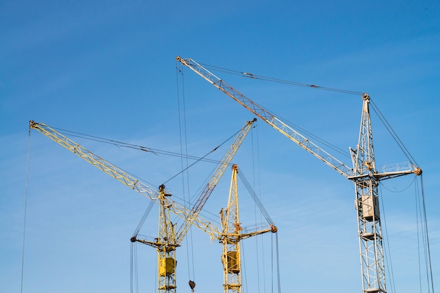 Grandi gru a torre contro il cielo blu. Immagine del primo piano dell'attrezzatura per l'edilizia con lo spazio della copia. Costruire della città.