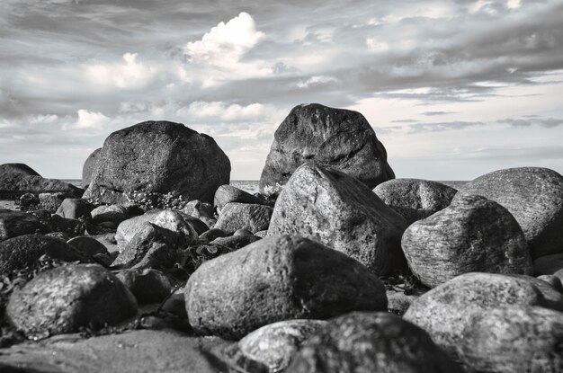 Grandi pietre in bianco e nero scattate sulla spiaggia di pietra di fronte al mare con le nuvole nel cielo