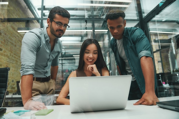 Grandi risultati gruppo di tre giovani dipendenti che guardano lo schermo del laptop e sorridono mentre