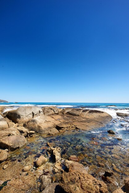 Grandi rocce nell'oceano o nell'acqua di mare con uno sfondo di cielo blu Bellissimo paesaggio con vista panoramica sulla spiaggia con massi in una giornata estiva Rilassante scenario del mare o della natura