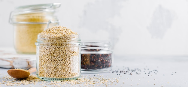 Grani crudi della quinoa in barattolo Cibo vegetariano sano sul tavolo da cucina grigio. Messa a fuoco selettiva.