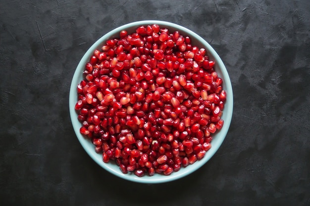 Grani di melograno rosso in un piatto su un tavolo nero.