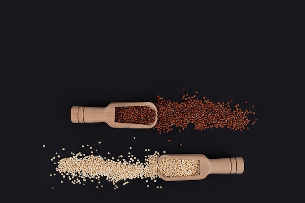 Grani di quinoa bianchi e rossi biologici crudi in cucchiai di legno su sfondo nero