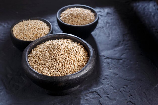 Grani di quinoa con cucchiaio e ciotola su sfondo nero