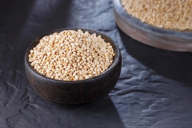 Grani di quinoa con cucchiaio e ciotola su sfondo nero