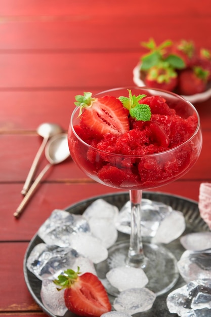 Granita alla fragola o sorbetto di frutti di bosco freschi in vetro su vecchio sfondo tavolo in legno rosso Texture di gelato o sorbetto Gelato con fragola e menta Ricetta sorbetto Trattamento estivo Messa a fuoco selettiva