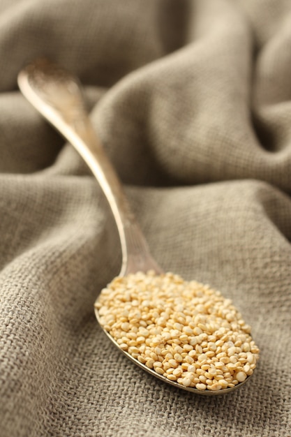 Grano della quinoa in cucchiaio del metallo su fondo della tela di sacco