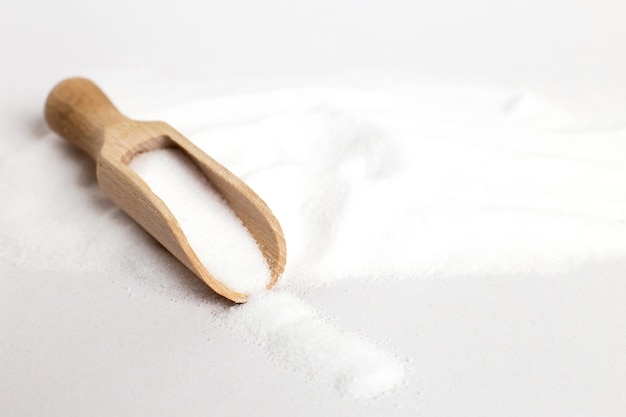 Grano di sale in vista dall'alto del cucchiaio di legno su uno sfondo bianco, piatto disteso.