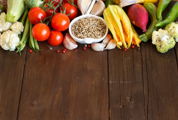 Grano di segale crudo in una ciotola e verdure sulla tavola di legno