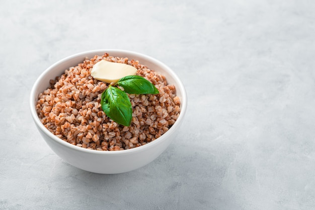 Grano saraceno bollito con basilico e burro su un muro grigio. Vista laterale, copia dello spazio. Cibo dietetico sano.