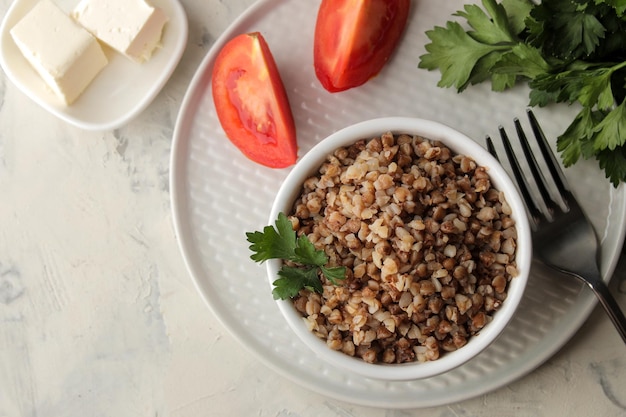 Grano saraceno. Cereali di porridge con prezzemolo in una ciotola di ceramica bianca e pomodoro su un tavolo luminoso. colazione, cibo sano. vista dall'alto