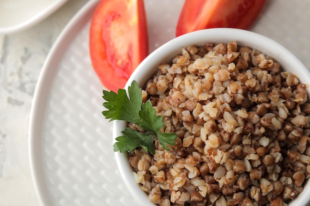 Grano saraceno. Cereali di porridge con prezzemolo in una ciotola di ceramica bianca e pomodoro su un tavolo luminoso. colazione, cibo sano. vista dall'alto