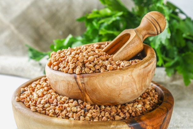 Grano saraceno crudo in ciotole di legno e un mestolo su tela di sacco su un fondo di legno. Cibo dieta sana