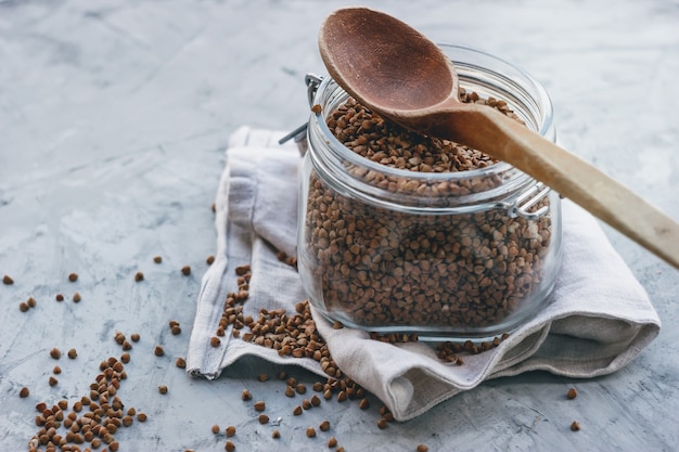 grano saraceno in un barattolo di vetro con un cucchiaio di legno, su una superficie grigia chiara. Spazio per il testo