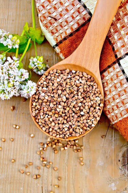 Grano saraceno in un cucchiaio con grano saraceno fiore, centrino a scacchi marrone su uno sfondo di assi di legno