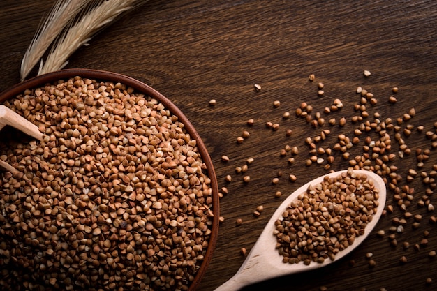 Grano saraceno in una ciotola di legno su un tavolo di legno vicino alle spighe di grano. cucchiaio di legno con grano saraceno