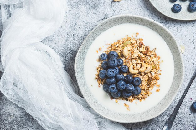 Granola con yogurt e mirtilli in un piatto su uno sfondo grigio