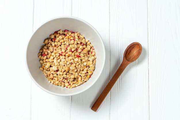 Granola del grano bianco in una ciotola bianca in una composizione con un cucchiaio su fondo di legno bianco.