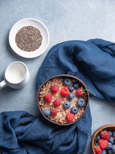 Granola energetico con lampone, mirtillo, semi di chia e latte vegano nella ciotola di cocco su sfondo blu. Vista dall'alto