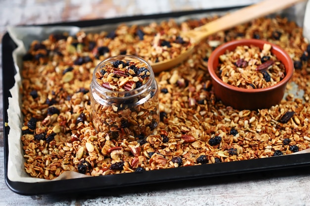 Granola fatta in casa appena fatta su una teglia con un cucchiaio di legno e vasetti