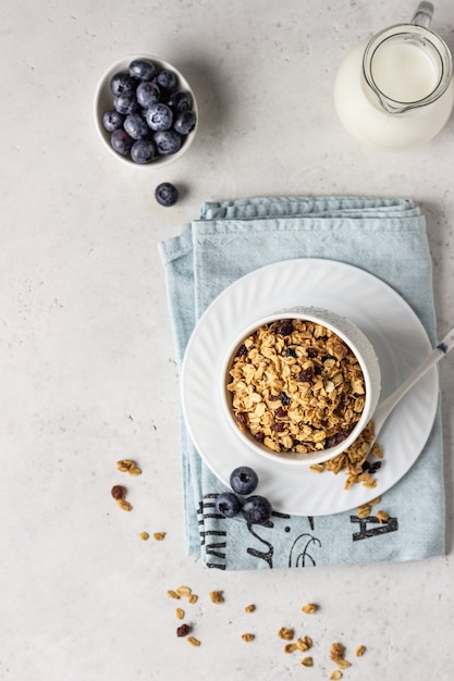 Granola fatta in casa in una ciotola in ceramica bianca con uvetta, mirtilli e latte. Ingredienti salutari per la colazione