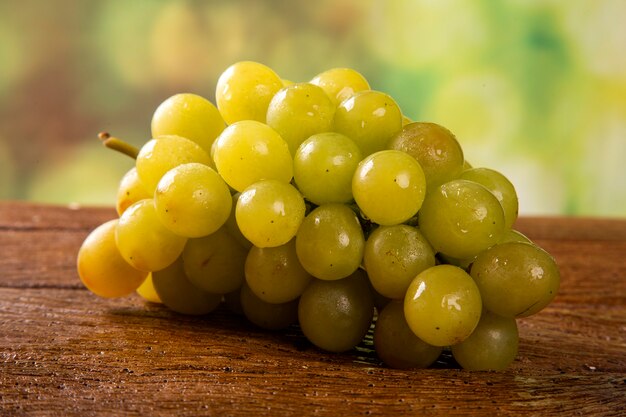 Grappolo d'uva verde, frutti di autunno, simbolo di abbondanza su fondo di legno rustico.