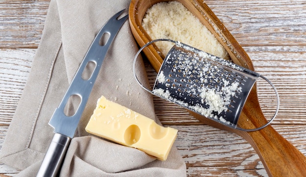 Grattugia per formaggio e formaggio con coltello su fondo di legno tovagliolo