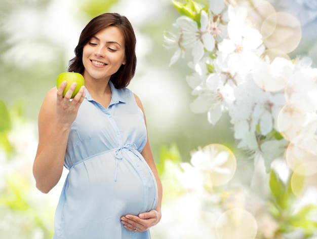 gravidanza, alimentazione sana, cibo e concetto di persone - donna incinta felice che tiene mela verde su sfondo di fiori di ciliegio primaverile naturale
