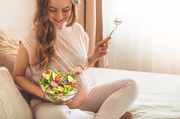 Gravidanza e sana alimentazione biologica. Donna incinta che gode dell'insalata di verdure fresche a letto, spazio libero