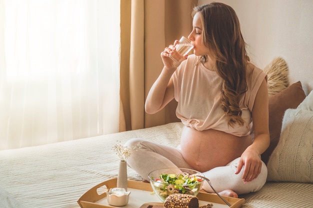 Gravidanza e sana alimentazione biologica. Donna incinta che gode dell'insalata di verdure fresche a letto, spazio libero