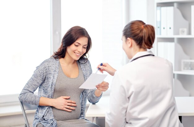 gravidanza, ginecologia, medicina, assistenza sanitaria e concetto di persone - medico ginecologo con prescrizione e incontro di donna incinta in ospedale