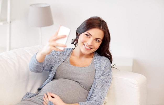 gravidanza, maternità, tecnologia, persone e concetto di aspettativa - felice donna incinta con smartphone che prende selfie a casa