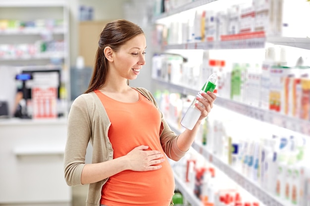 gravidanza, medicina, farmacia, assistenza sanitaria e concetto di persone - donna incinta felice che sceglie una lozione anti smagliature in farmacia
