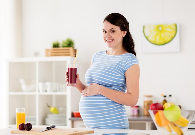 gravidanza, persone e concetto di alimentazione sana - donna incinta sorridente felice che beve succo o frullato nella cucina di casa