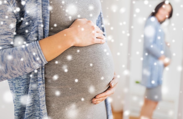 gravidanza, persone, inverno, natale e concetto di aspettativa - primo piano di felice donna incinta con grande pancia che guarda allo specchio a casa sopra la neve