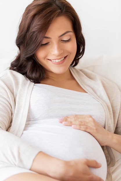 gravidanza, riposo, persone e concetto di aspettativa - felice donna incinta sdraiata sul letto e che tocca la pancia a casa