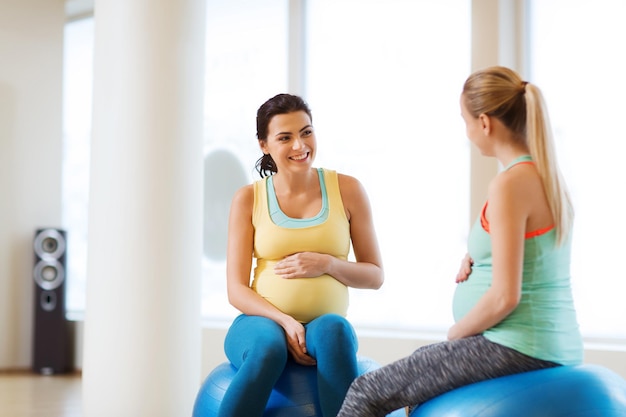 gravidanza, sport, fitness, persone e concetto di stile di vita sano - due donne incinte felici che si siedono e parlano sulle palle in palestra