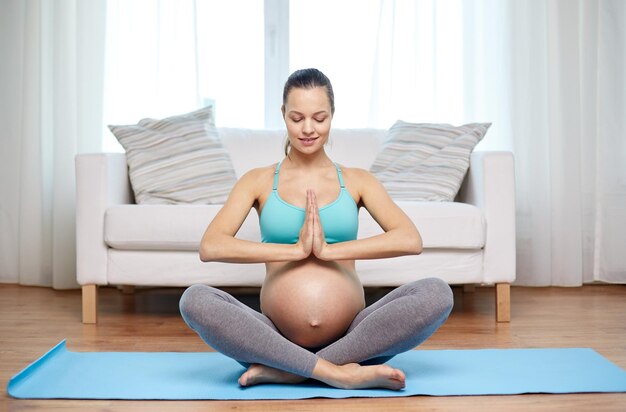 Gravidanza, sport, yoga, persone e concetto di stile di vita sano - donna incinta felice che medita a casa