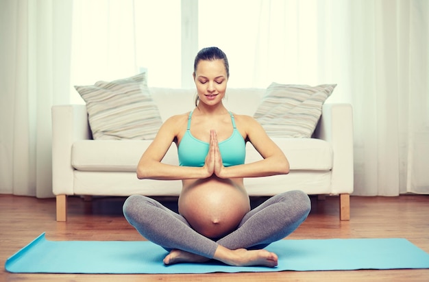 Gravidanza, sport, yoga, persone e concetto di stile di vita sano - donna incinta felice che medita a casa