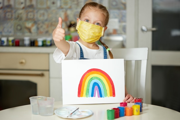 Grazie a NHS. Ragazzo in maschera protettiva che dipinge l'arcobaleno durante la quarantena Covid-19 a casa. focolaio di coronavirus covid-19.
