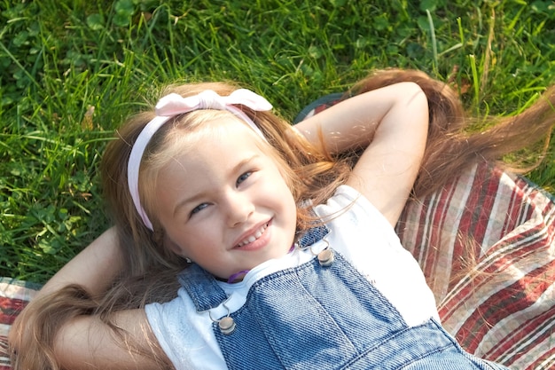 Graziosa bambina con gli occhi chiusi sdraiata sull'erba verde in estate facendo un pisolino.